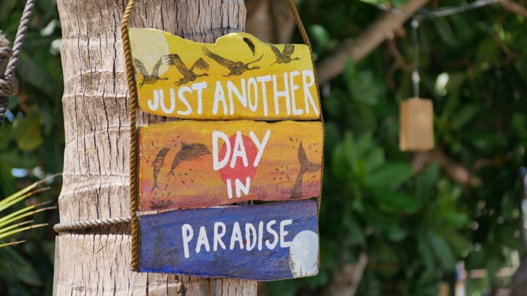 Wooden "Just another day in paradise" sign on a tropical island, where travellers can book HIV tests after PEP