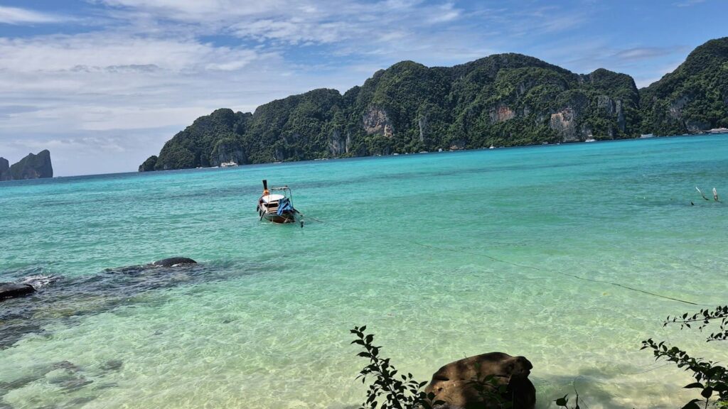 Longtail boat moored in a turquoise bay, illustrating island travel for PEP between Koh Phangan, Koh Tao and Koh Samui