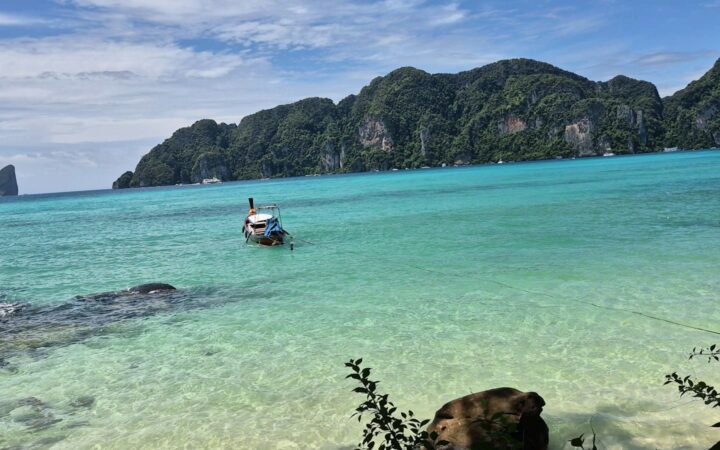 Longtail boat moored in a turquoise bay, illustrating island travel for PEP between Koh Phangan, Koh Tao and Koh Samui