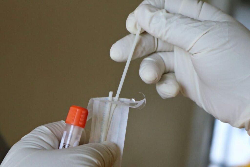 Gloved hand holding a swab and specimen tube, used for chlamydia and gonorrhoea STD testing
