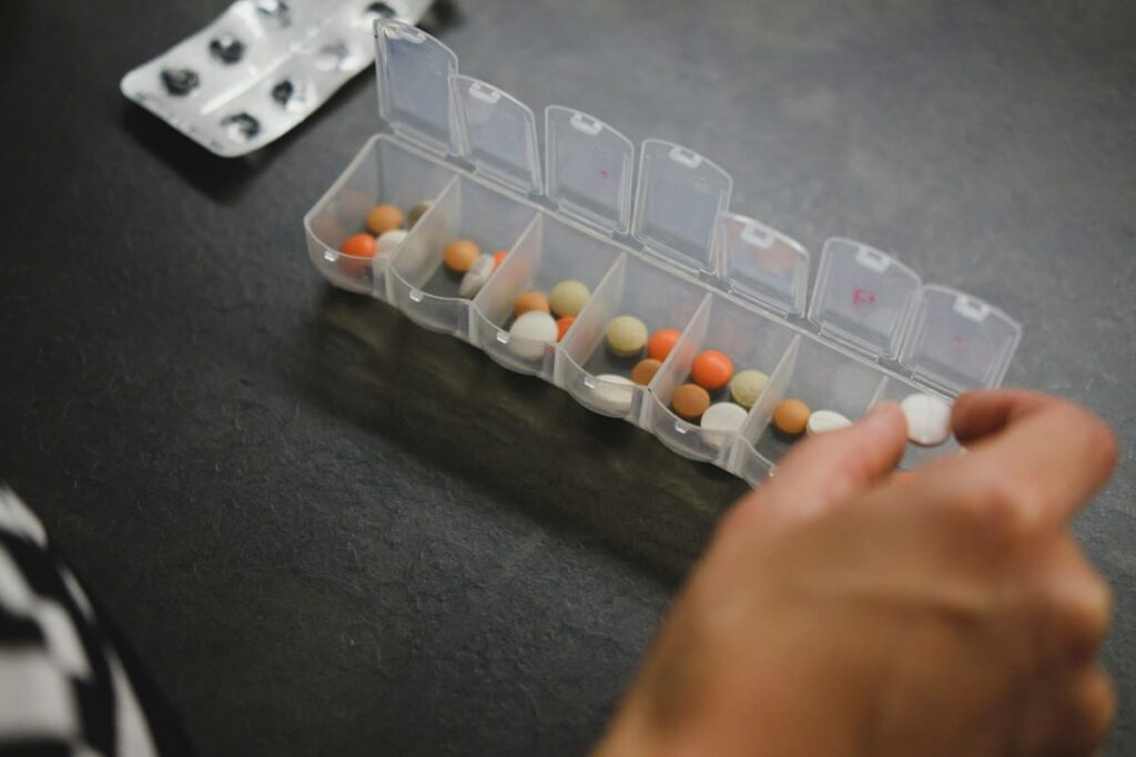 Hand taking a tablet from a weekly pill box, illustrating a daily HIV PrEP routine and its monthly cost