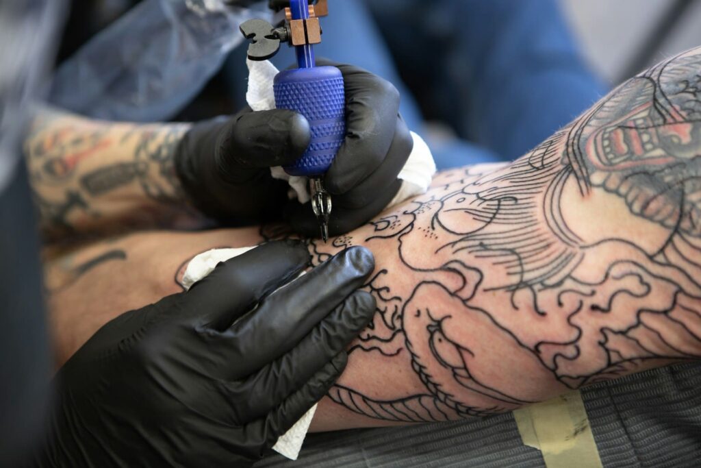 Tattoo artist in black gloves working on a sleeve tattoo, representing safe tattooing and low HIV risk