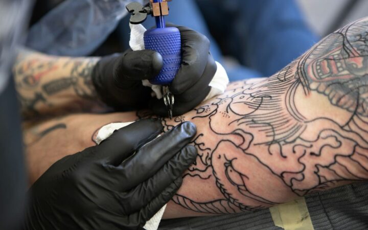 Tattoo artist in black gloves working on a sleeve tattoo, representing safe tattooing and low HIV risk
